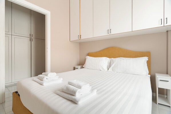 A neatly made bed with white linens and towels, a wooden headboard, and a white nightstand. - Brera Apartments in Sant'Ambrogio (Milan)