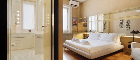 Habitación de hotel moderna con una cama grande, baño con espejo e iluminación, y vista a la ciudad.