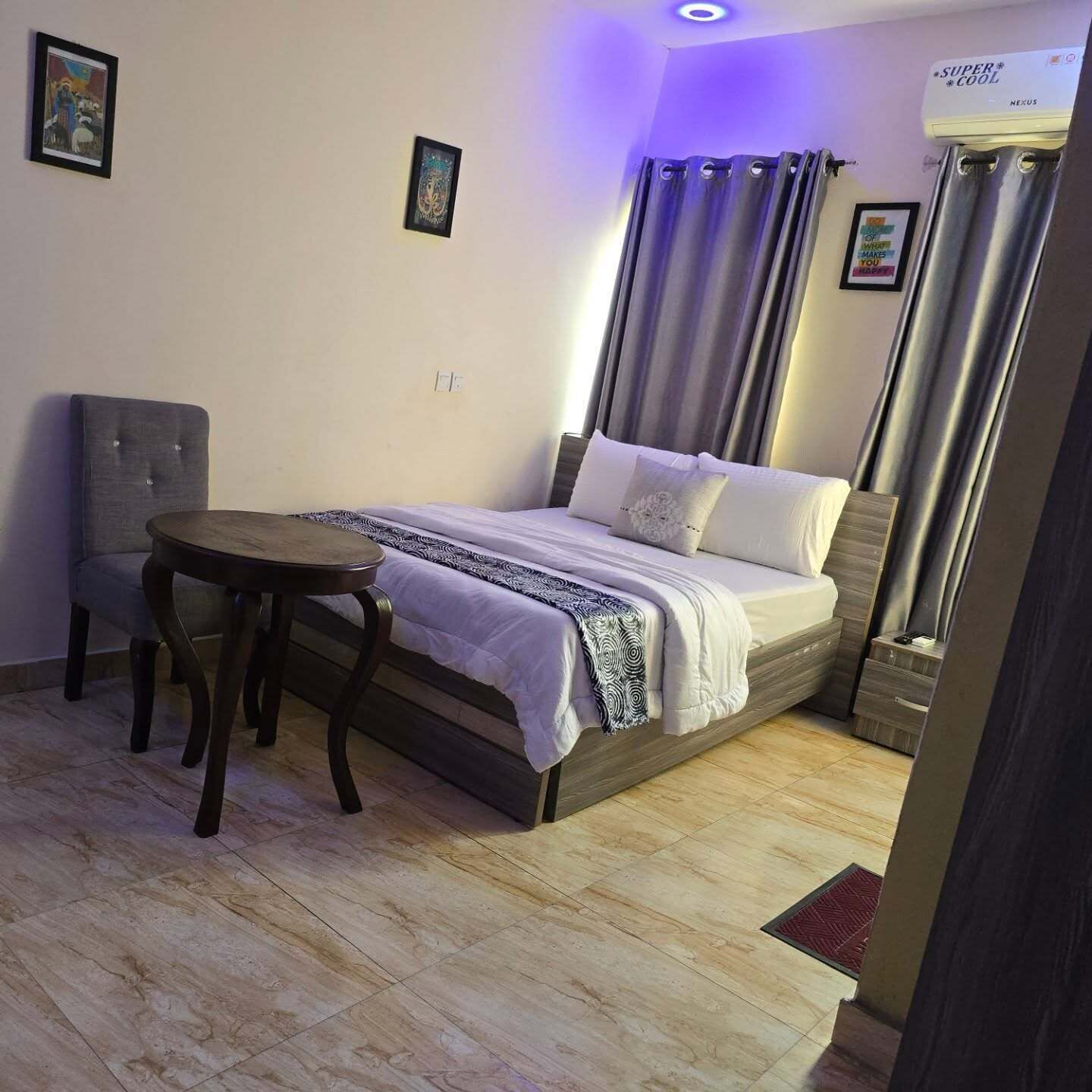 Ein Schlafzimmer mit Bett, Sessel, einem kleinen Tisch und Deckenleuchte.