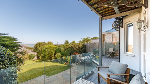 Ein Balkon mit Glastrennwand, einem Holztisch und zwei Stühlen.