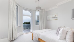 Ein Schlafzimmer mit einem großen Bett, weißen Vorhängen, Blick ins Freie und einer Deckenleuchte.