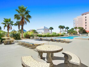 A poolside area with lounge chairs, a pool, palm trees, and a building with balconies. - The Indies #209 | Quiet Beach, Pool, Hot Tub, Gym, Rooftop Deck (Gulf Shores)