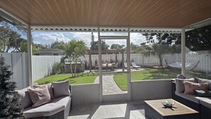 An outdoor patio with wicker furniture, a wooden ceiling, and a view of a backyard. - Charming Beach Cottage with Hot Tub only 1 Mile to Gulf! (Naples)