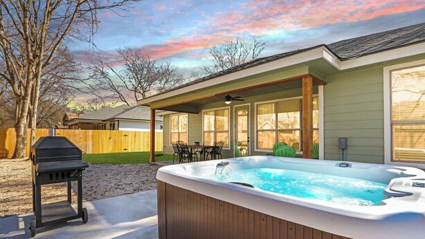 Ein Garten mit Whirlpool, Grill und einer Terrasse mit Stühlen und Tisch.