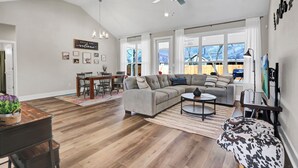 Ein geräumiges Wohnzimmer mit einem Ecksofa, einem Essbereich mit Holztisch und Stühlen sowie einem großen Fenster mit Blick auf Bäume.