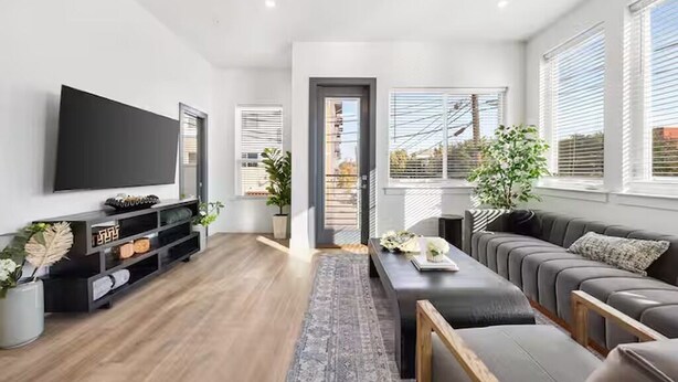 Uma sala de estar moderna com televisão de tela plana, um sofá cinza, uma mesa de centro de madeira e um tapete cinza.