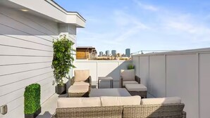 Terraço no telhado com móveis de vime, um vaso de planta e vista para o horizonte da cidade.