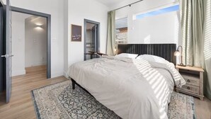 Quarto com cama, mesas de cabeceira, tapete estampado e uma porta que dá para outro espaço.