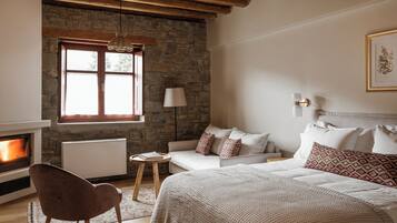 A cozy bedroom with a stone wall, a fireplace, a bed with patterned pillows, a side table, and a chair.