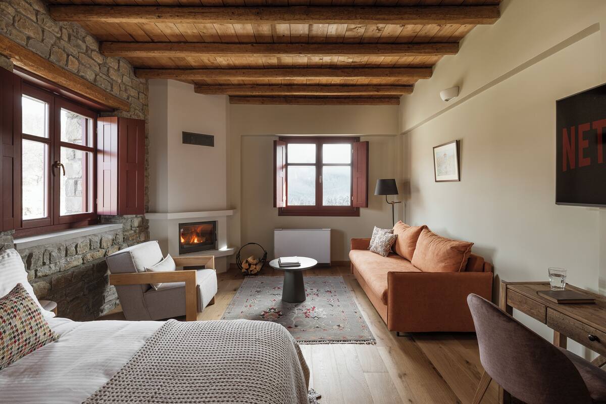 A cozy living room with a fireplace, wooden beams, stone walls, and a comfortable seating area.