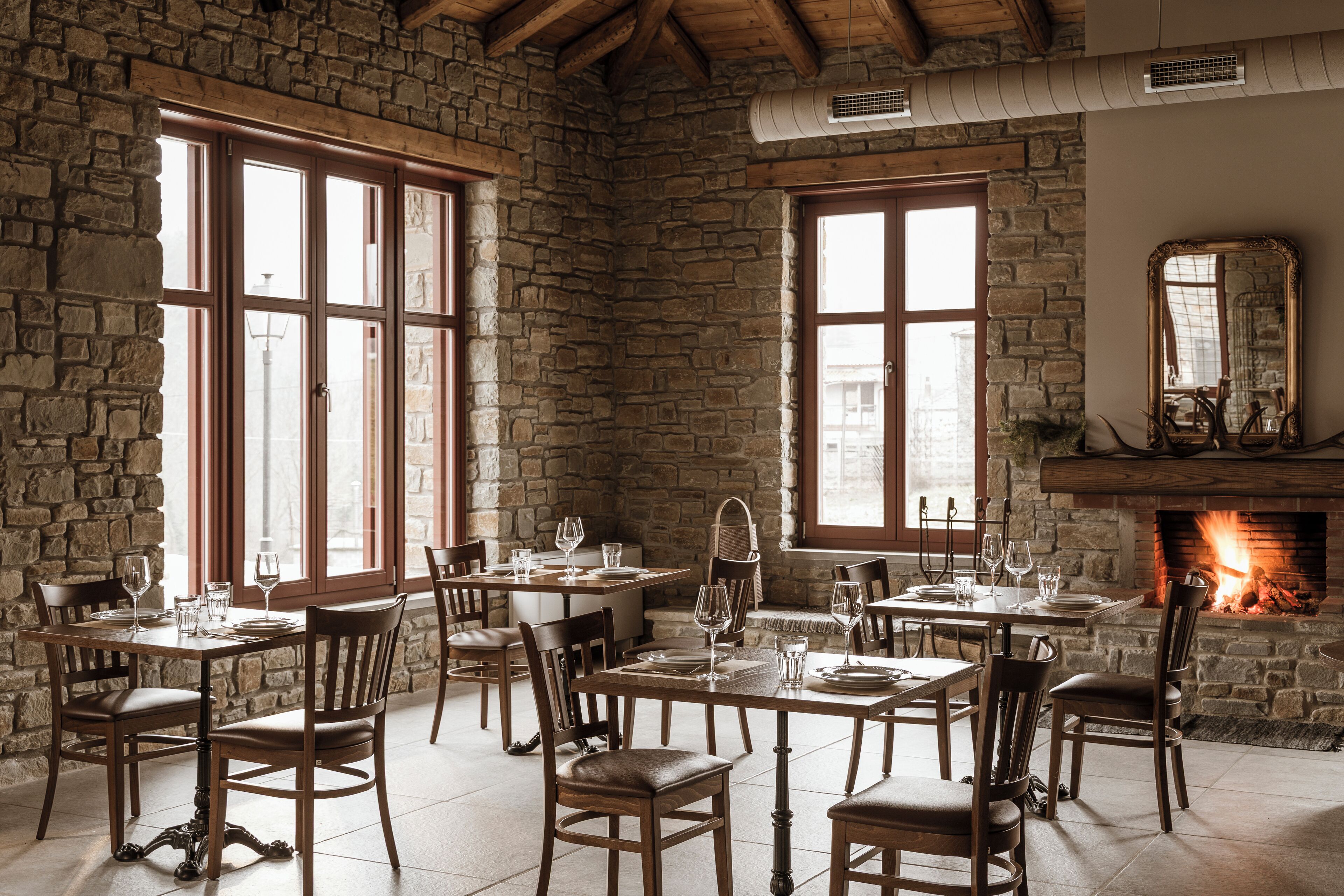Un comedor rústico con paredes de piedra, mesas y sillas de madera, y una chimenea.