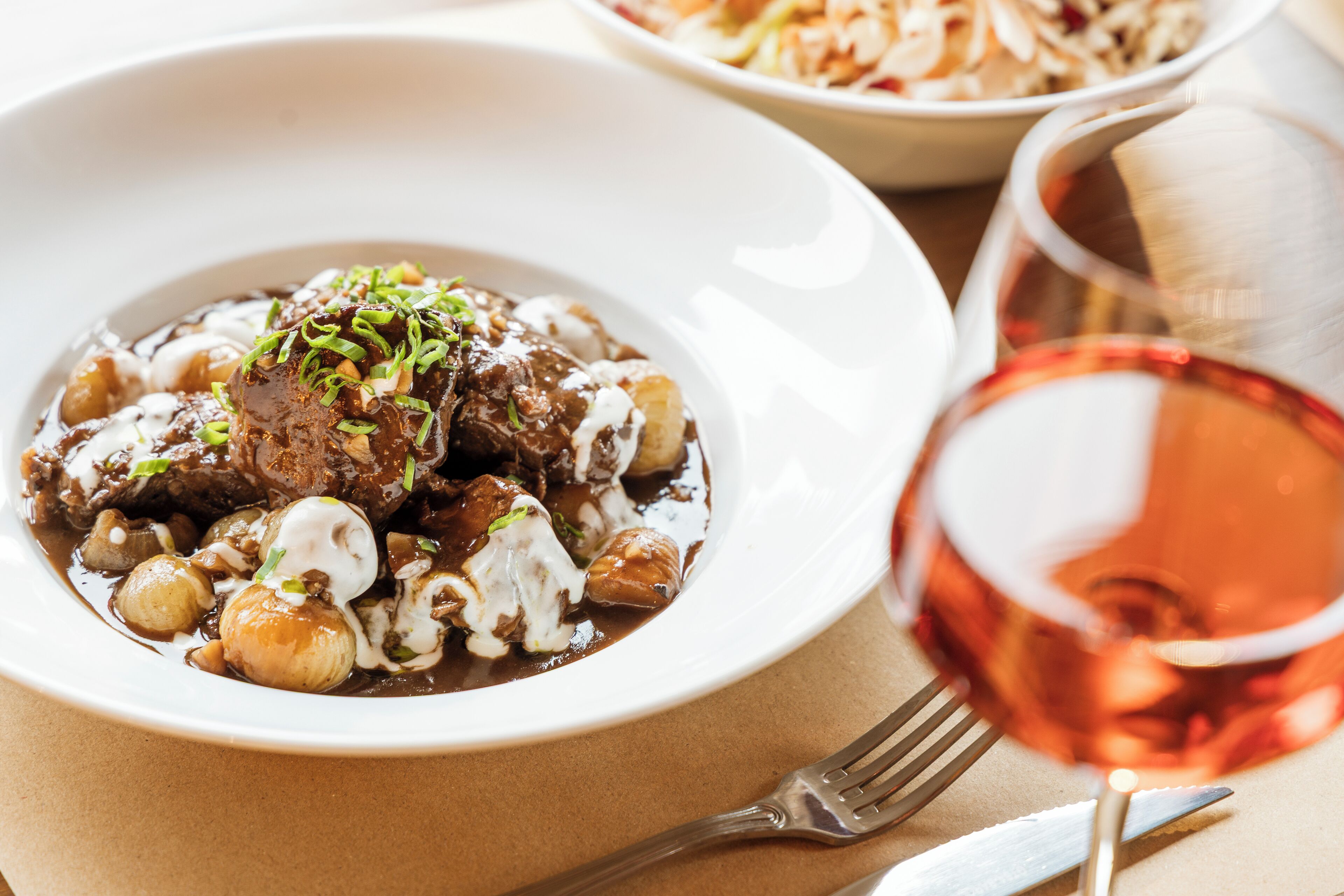 Um prato de ensopado de carne com cogumelos e um copo de vinho tinto.