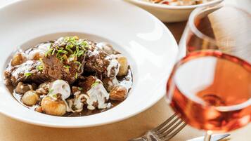 Um prato de ensopado de carne com cogumelos e um copo de vinho tinto.