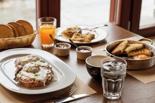 Desayuno con tostadas, huevos y jugo de naranja sobre una mesa de madera.