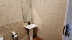 Un bagno con piastrelle color crema, un lavandino bianco, uno specchio e un water.