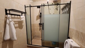 Cabina doccia in vetro con soffione a mano, porta in vetro e porta asciugamani con un asciugamano bianco.