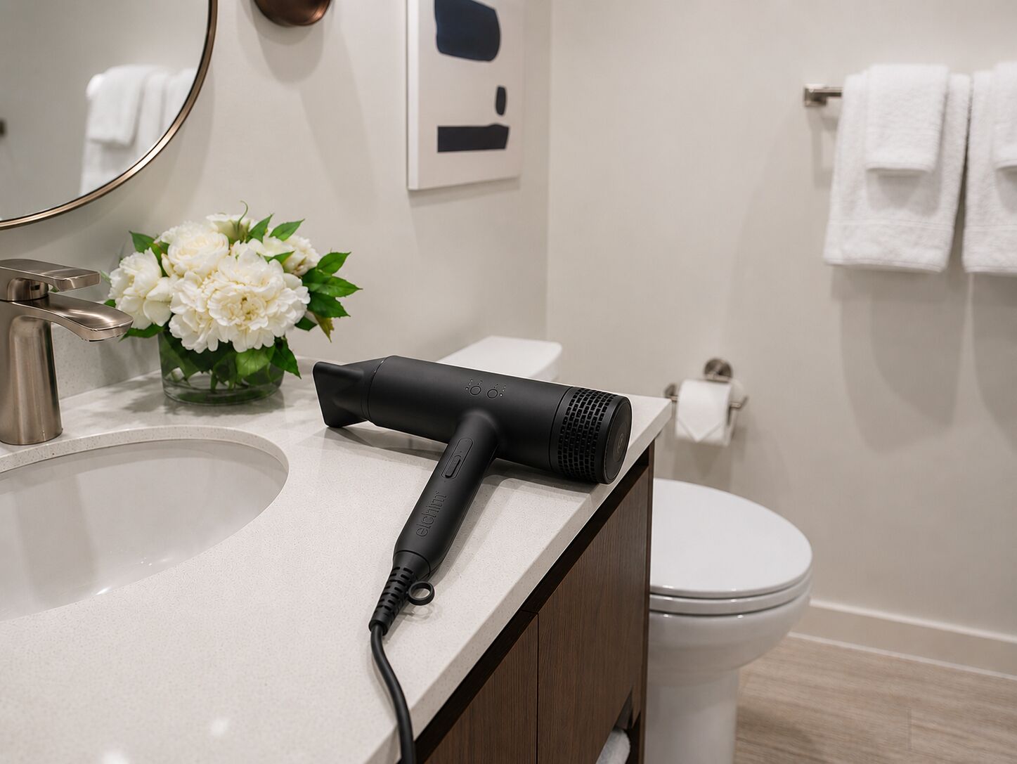 A bathroom with a sink, a hair dryer, a toilet, and a vase of flowers.