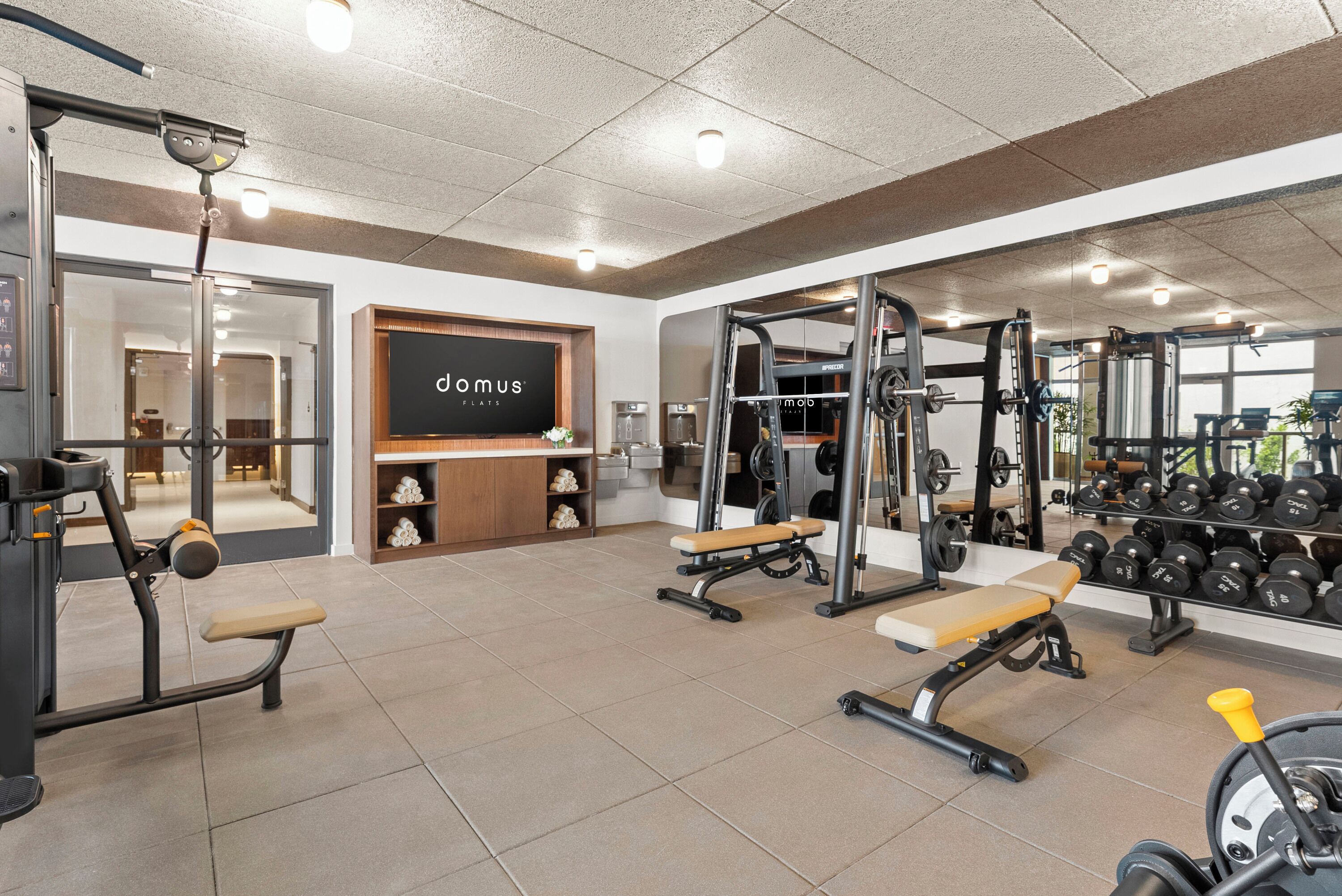 Une salle de sport équipée de matériel d’exercice, de bancs et d’un grand miroir fixé au mur.