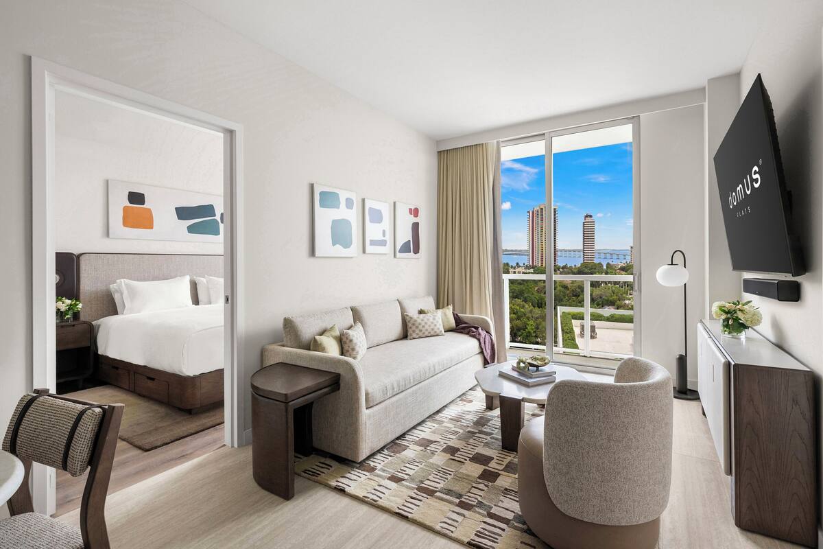 Una habitación de hotel moderna con cama, sofá, sillón y televisor.