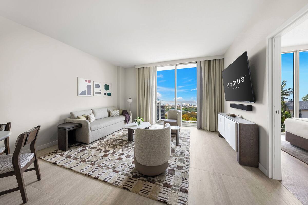 Una habitación de hotel moderna con sofá, sillón, mesa de comedor y televisor.
