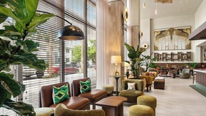Un moderno vestíbulo de hotel con zonas de estar, un bar y grandes ventanales con persianas.