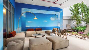 A modern outdoor seating area with sofas, ottomans, and rocking chairs, a round table, and a mural of a blue sky with clouds.