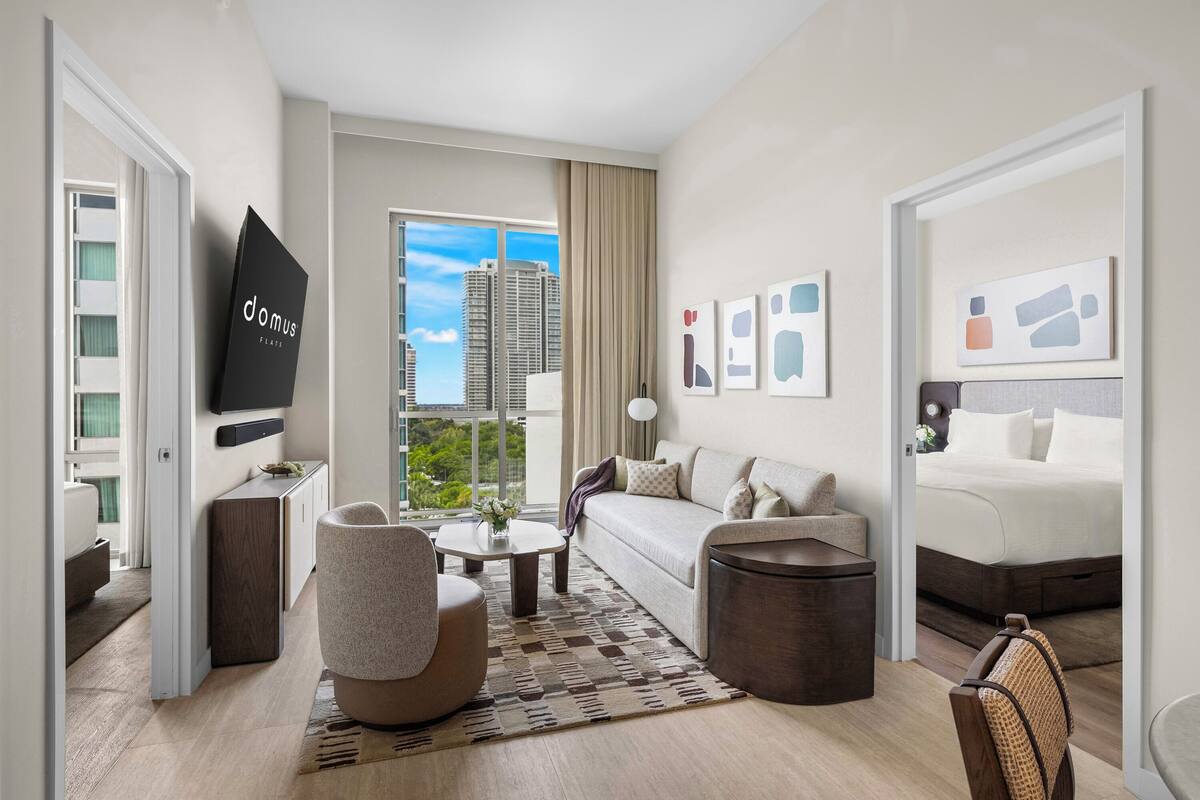 Una habitación de hotel moderna con sofá, sillón, mesa de centro y cama.