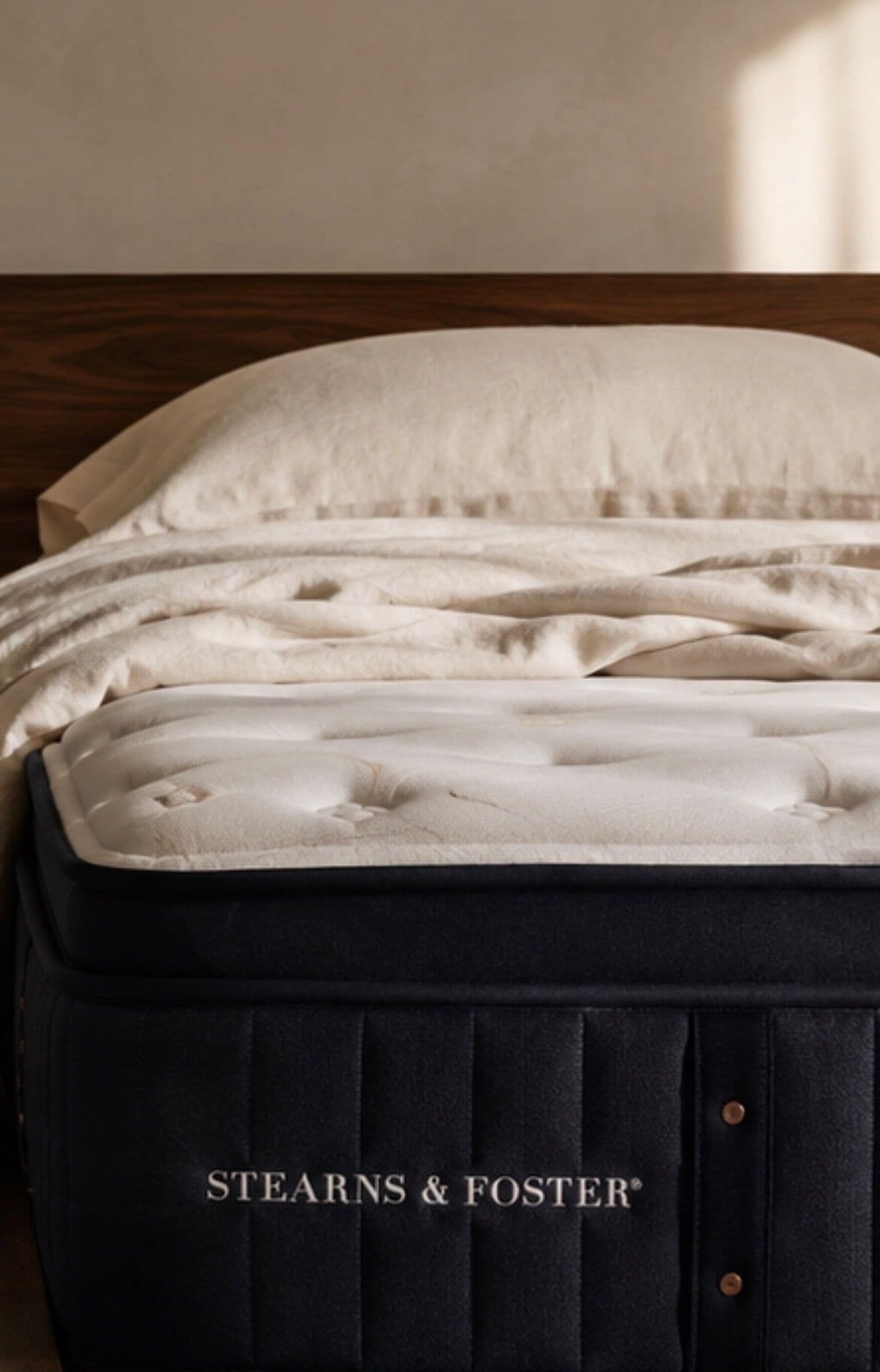 A dark-colored suitcase with a white pillow on top, labeled 'STEARNS & FOSTER.'