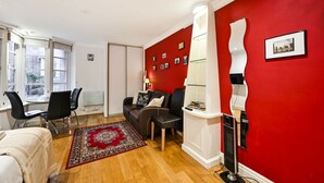 Un espace de vie compact agrémenté d’un mur d’accent rouge, d’un canapé en cuir noir, d’une petite table et d’un tapis à motifs rouges.