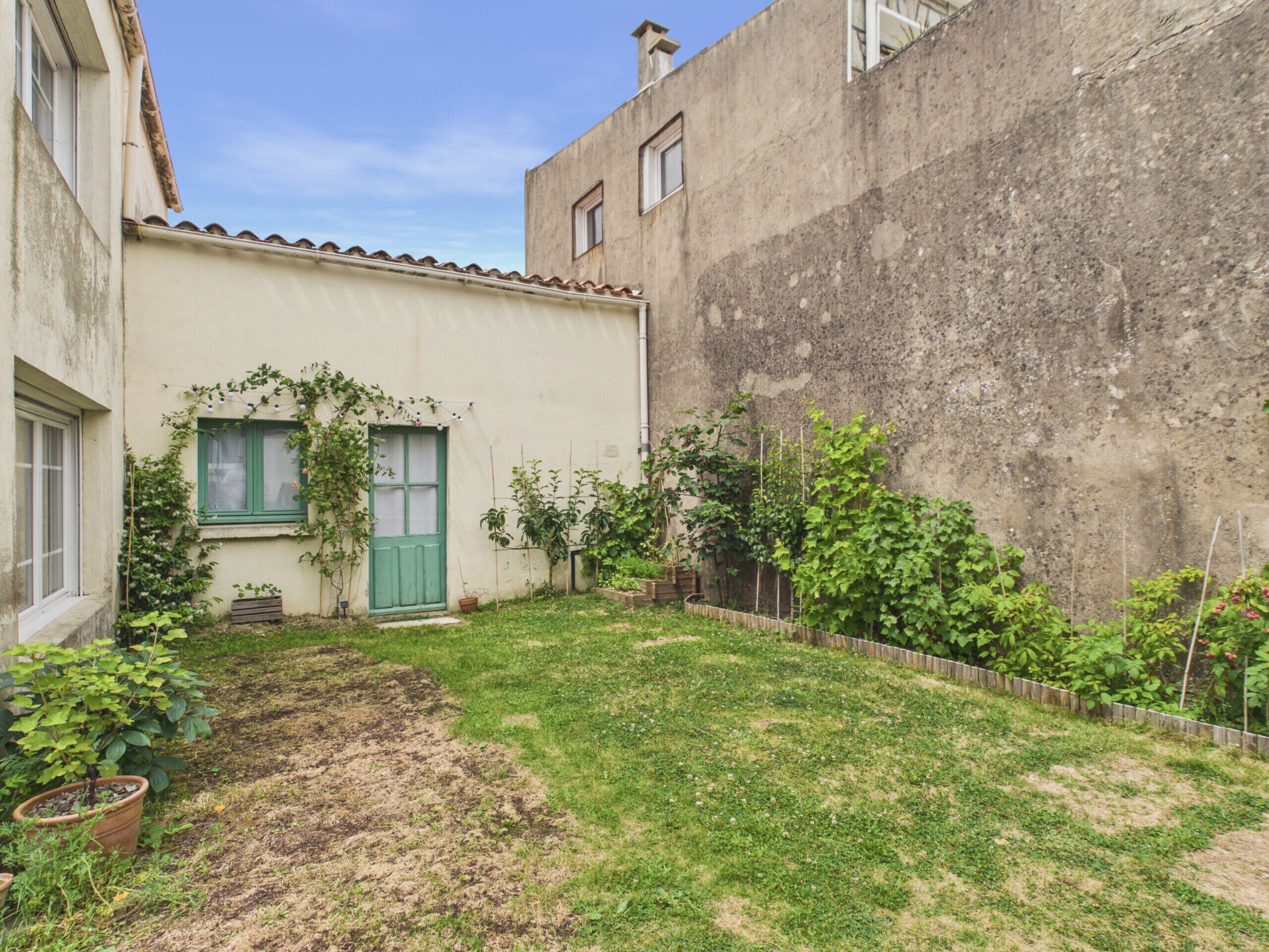 Un cortile con un piccolo giardino, una porta verde e una finestra con persiana bianca.