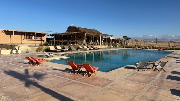 Una piscina amb gandules, un edifici amb teulada de palla i un paisatge de muntanyes al fons.