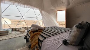 Una habitació tipus tenda amb llit, almoinos i vista al paisatge del desert.