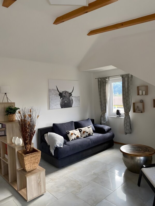 Ein modernes Wohnzimmer mit einem dunkelblauen Sofa, einem Holztisch und einer Decke mit freiliegenden Balken.