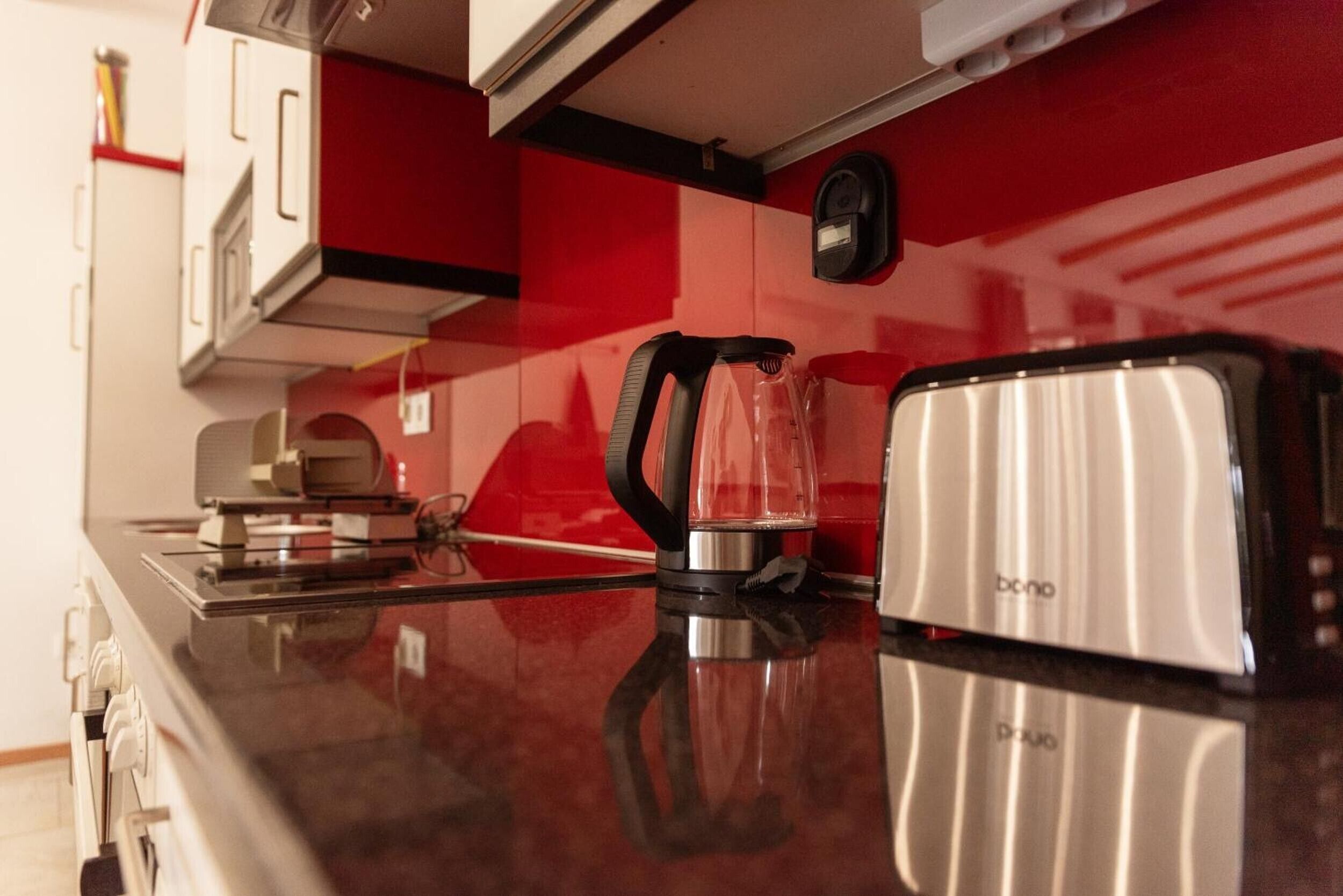 A kitchen with a black countertop, a glass kettle, and a silver toaster.