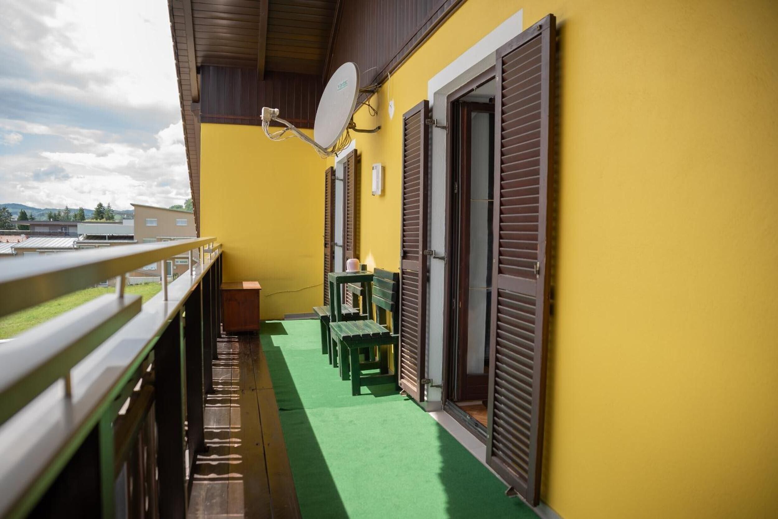 A balcony with a green carpet, wooden benches, and a satellite dish.