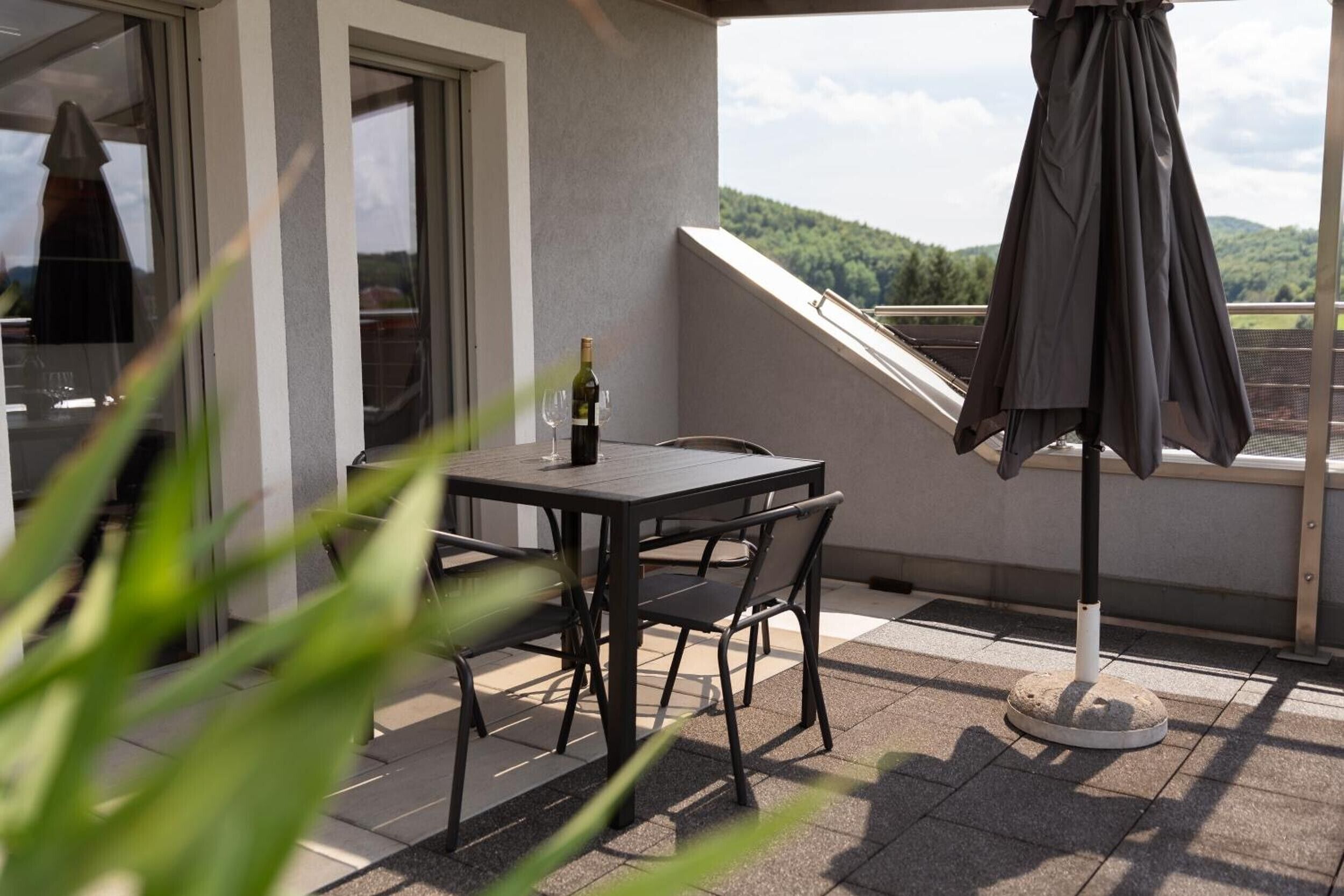 Ein Balkon mit Tisch, Stühlen, einer Weinflasche und einem Sonnenschirm.
