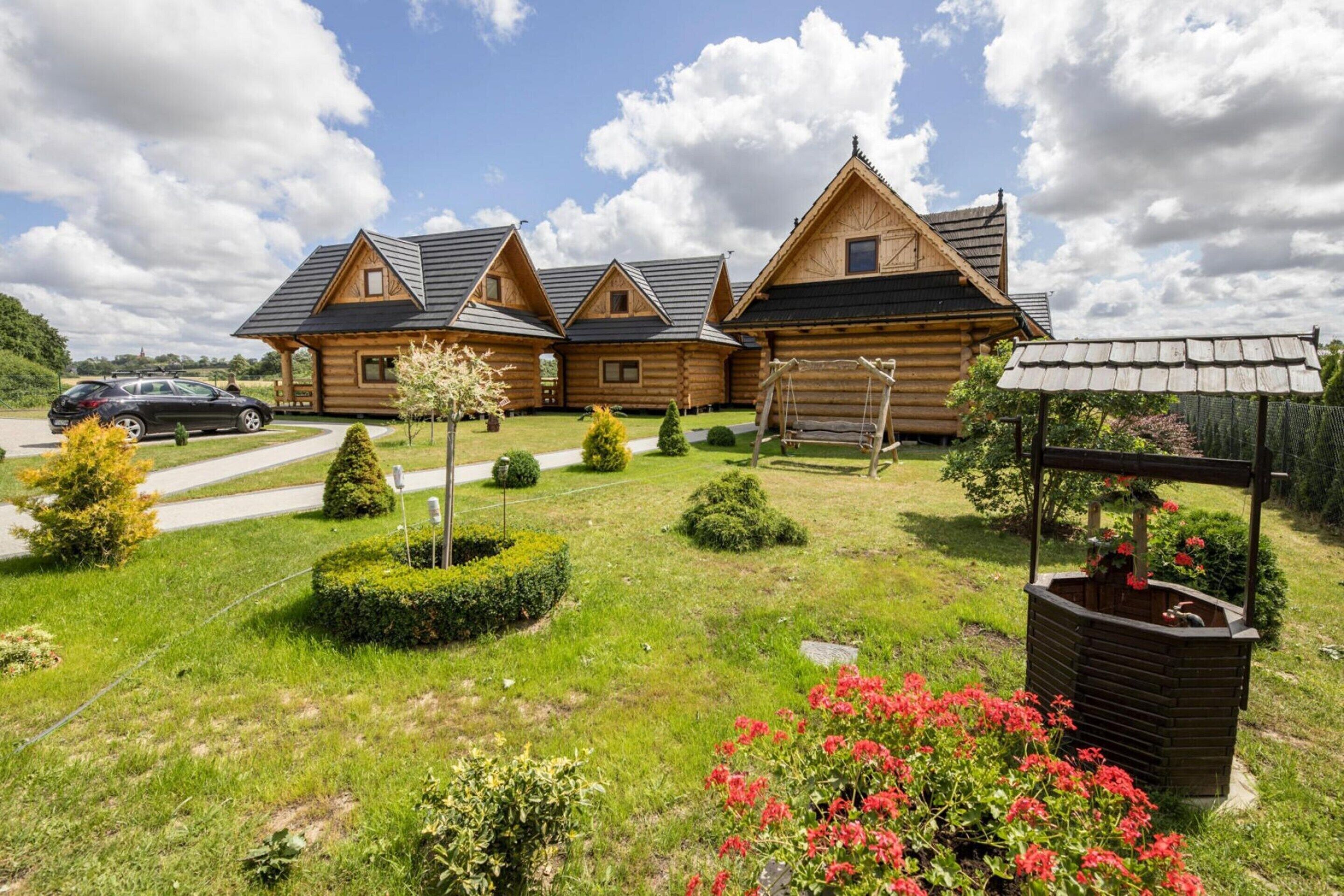 A log cabin with a sloped roof, a wooden porch, and a well-maintained garden with bushes and flowers.