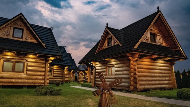 A row of log cabins with a central windmill, surrounded by well-maintained lawns and a pathway. - Comfortable, Large Holiday Homes With Terraces (Darlowo)