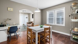 A dining area with a white table and wooden chairs, a pendant light, and a bookshelf with books and decorative items. - Chic 1BD 1 BA in quiet South City with easy access to I-44, near hospitals, parks, etc. Enjoy a cozy queen bed, full kitchen, fast WiFi, smart TV, and in-unit laundry. Ideal for solo travel, couples, or professionals. Free parking. No pets/smoking. (St. Louis)