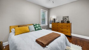 A bedroom with a bed, a wooden dresser, a ceiling fan, a window with blinds, and a small table with a lamp and decorative items. - Chic 1BD 1 BA in quiet South City with easy access to I-44, near hospitals, parks, etc. Enjoy a cozy queen bed, full kitchen, fast WiFi, smart TV, and in-unit laundry. Ideal for solo travel, couples, or professionals. Free parking. No pets/smoking. (St. Louis)