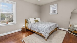 Um quarto com cama, ventoinha no teto, janela com persianas, mesa de cabeceira com abajur e espelho.