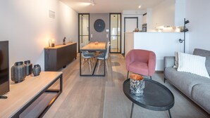 A modern living room with a TV, a dining area, and a kitchen. - Knokke City Centre Apartment for 6 (Knokke-Heist)
