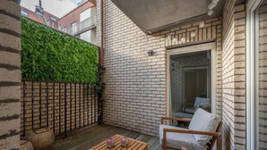 A wooden deck with a seating area, a glass door leading to a balcony, and a green wall. - Knokke City Centre Apartment for 6 (Knokke-Heist)