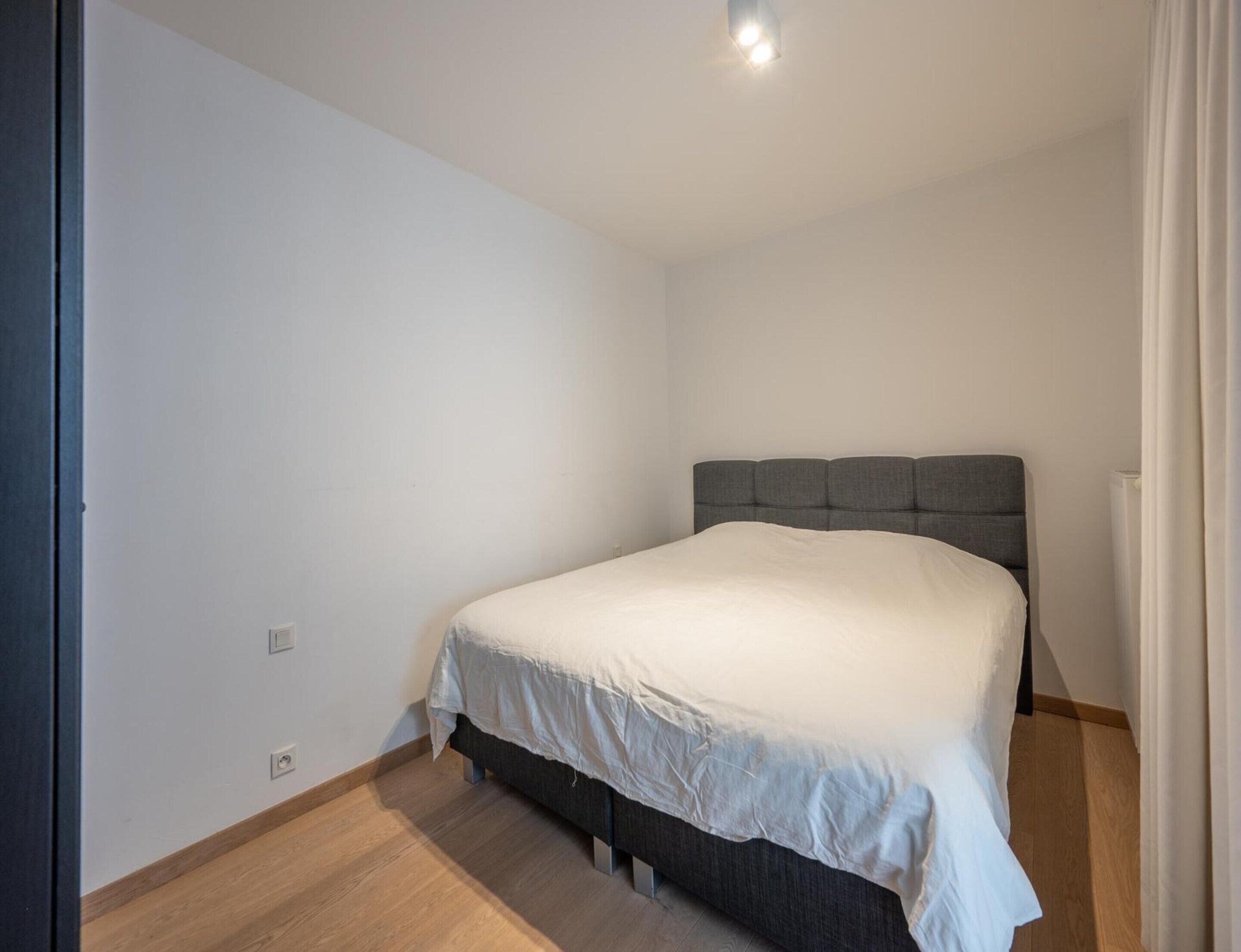Een slaapkamer met een bed, een lichtgekleurd hoofdeinde en een houten vloer.