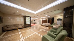 Un hall d’entrée spacieux avec un plafond haut, un comptoir d’accueil et plusieurs espaces aménagés pour s’asseoir.