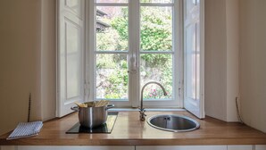 Une cuisine avec un plan de travail en bois, une casserole, un évier et une fenêtre donnant sur un paysage verdoyant et un bâtiment.