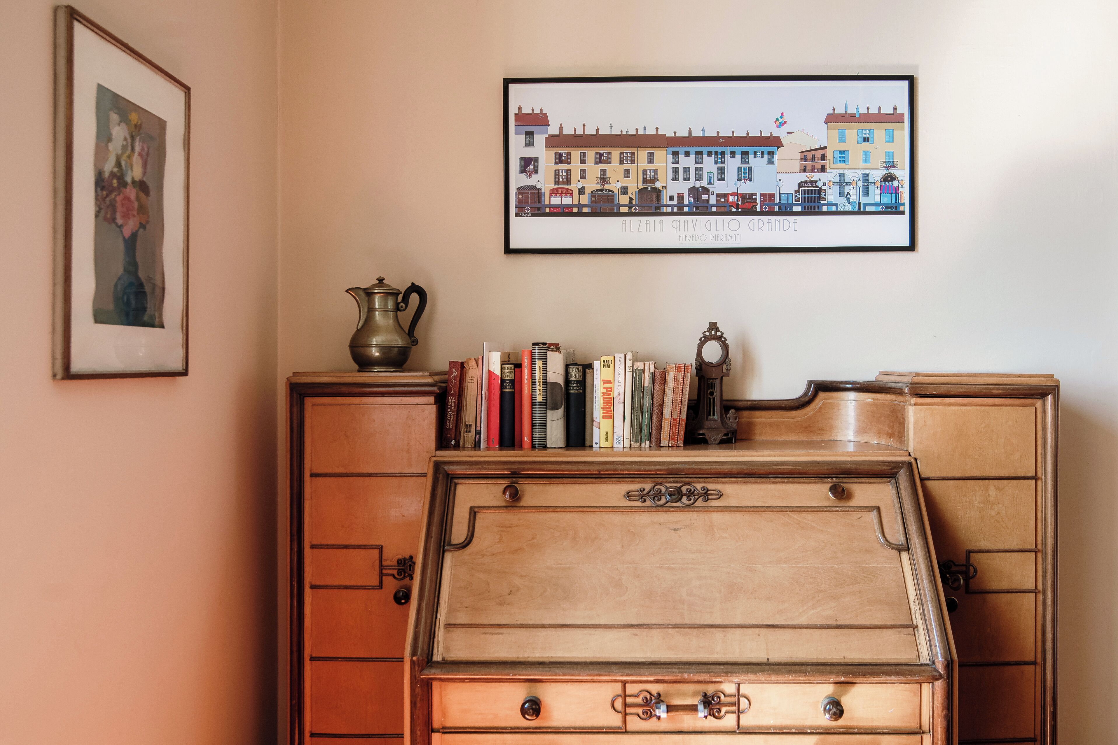 A wooden dresser with a flat top, a framed cityscape picture, and a vase with flowers on the wall.