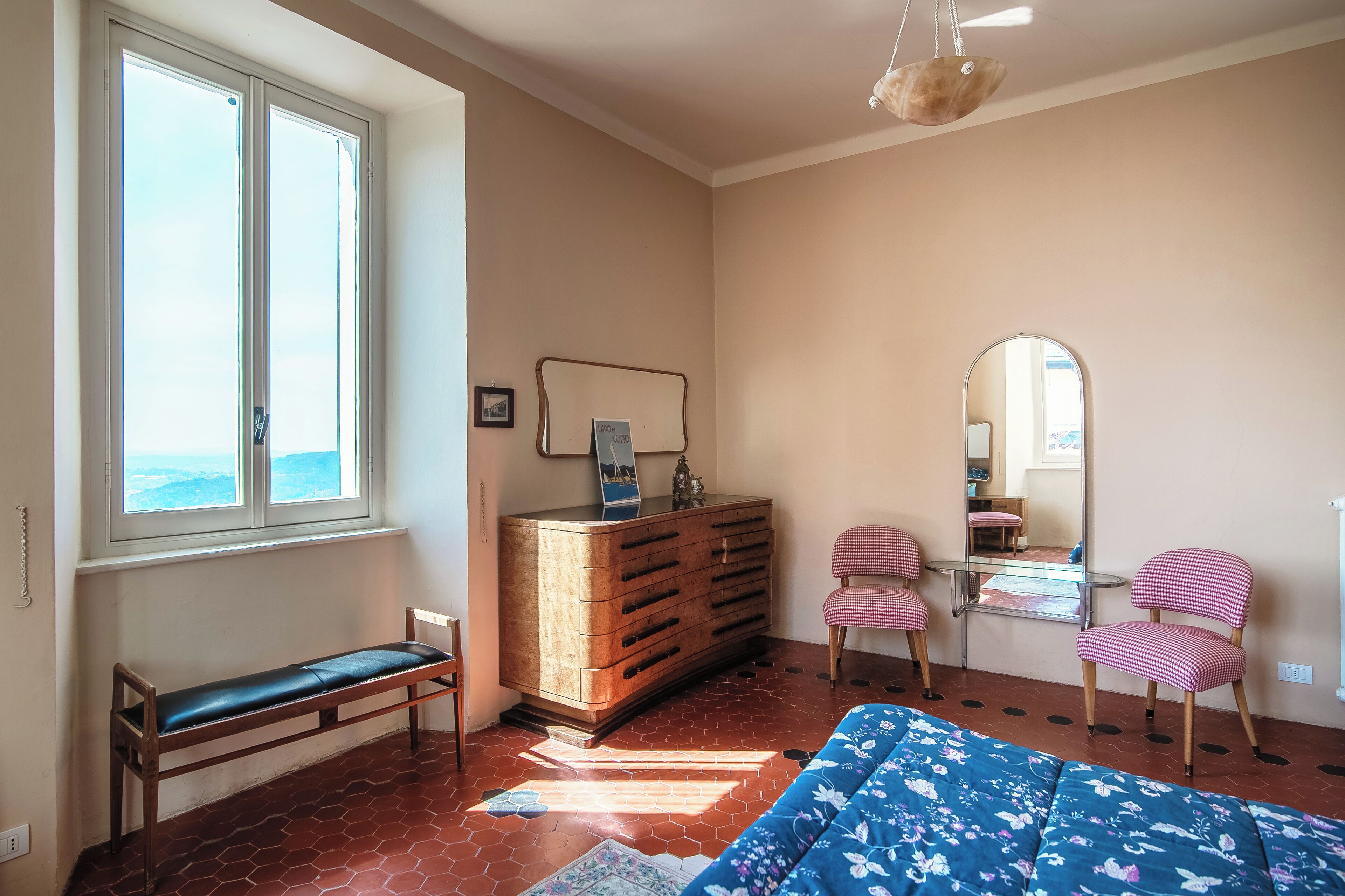 A room with a large window, a wooden bench, a dresser, a mirror, and a blue sofa.