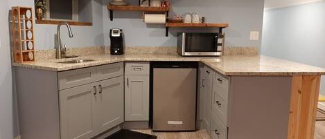 A compact kitchen with grey cabinets, a dishwasher, a microwave, and a coffee maker.