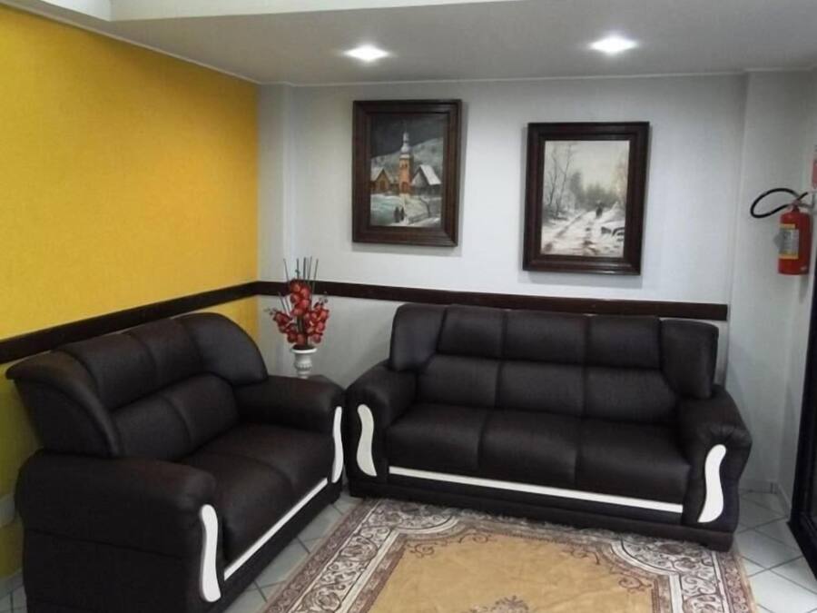 Una habitación con dos sofás de cuero negro con detalles blancos, un tapete estampado y dos cuadros en la pared.